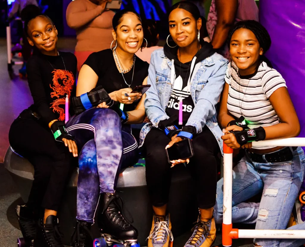 four black women sitting next to the roller rink smiling