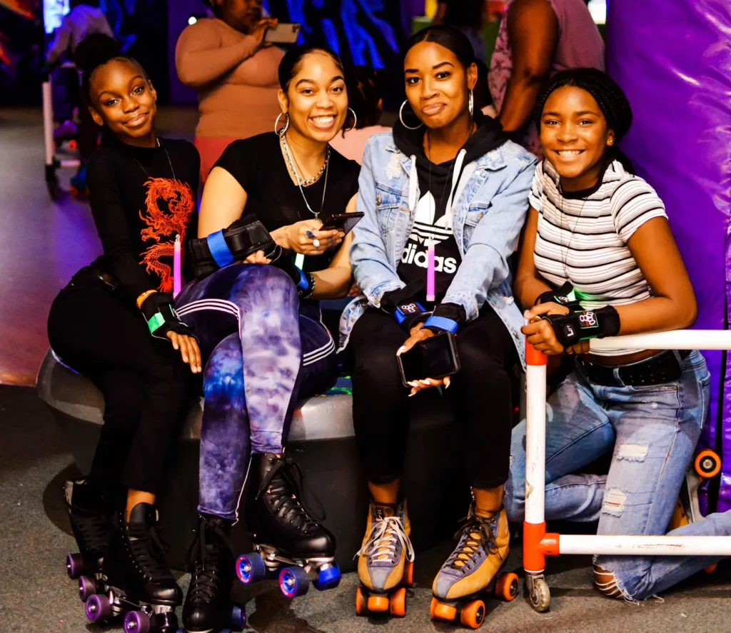 four black women sitting next to the roller rink smiling