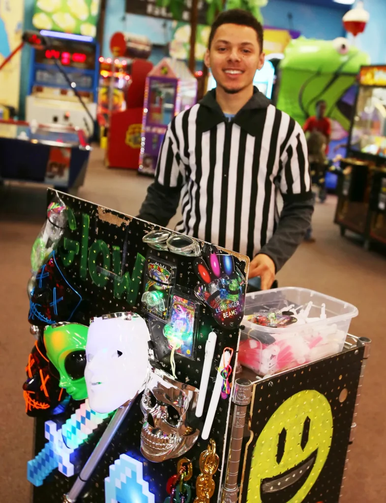 male staff member wearing a referee shirt working at a cart with glow in the dark items