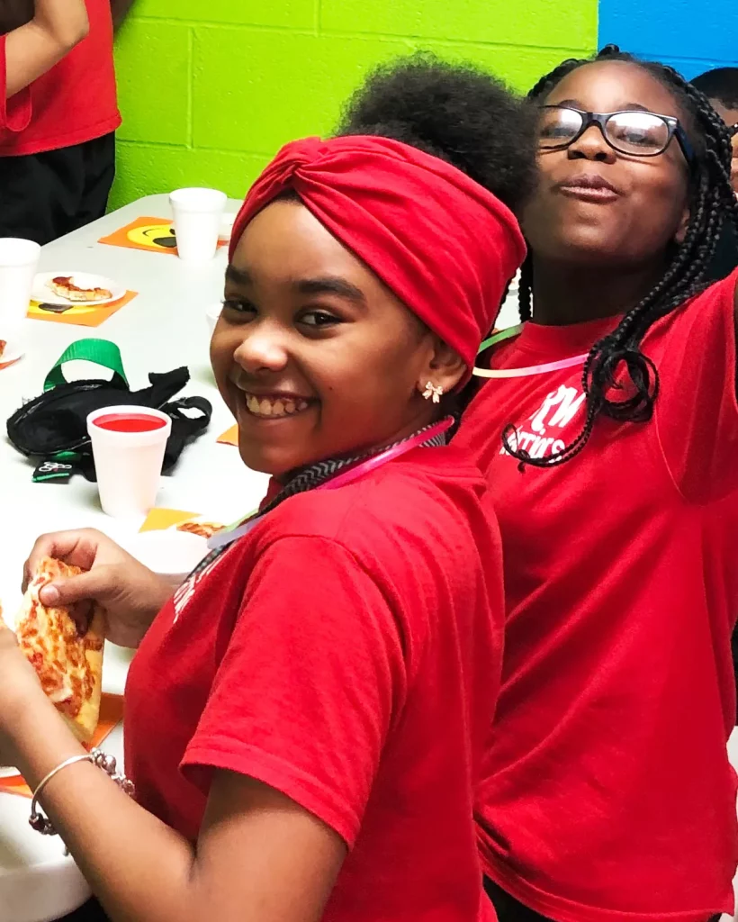 two girls in red shirts smiling and eating pizza