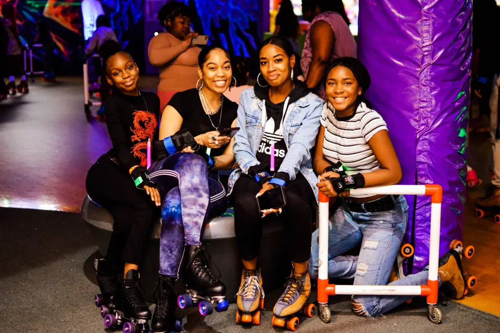 four black women sitting next to the roller rink smiling