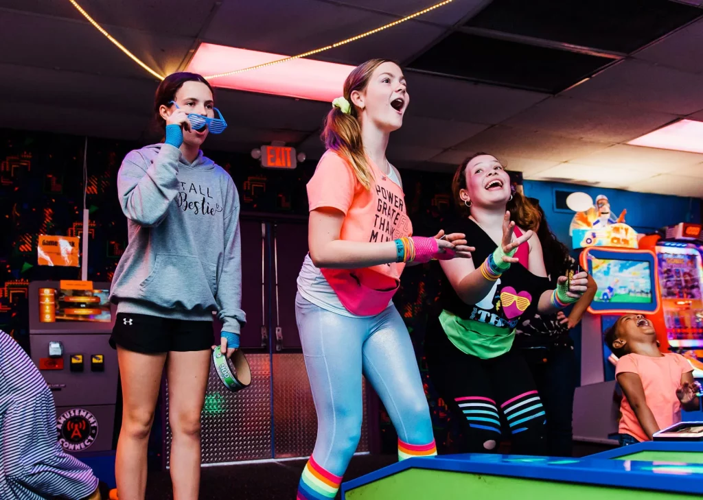 three teen girls dressed in retro 1980's attire playing games and laughing
