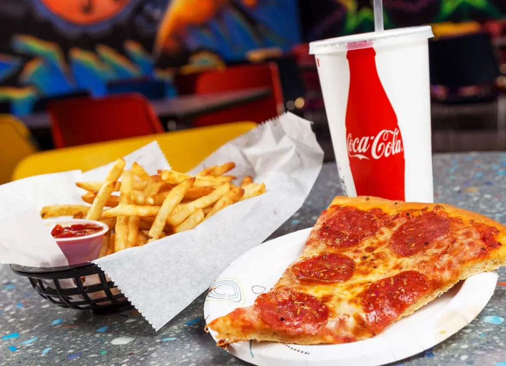 close up of a piece of pepperoni pizza, side of fries with ketchup and a soft drink
