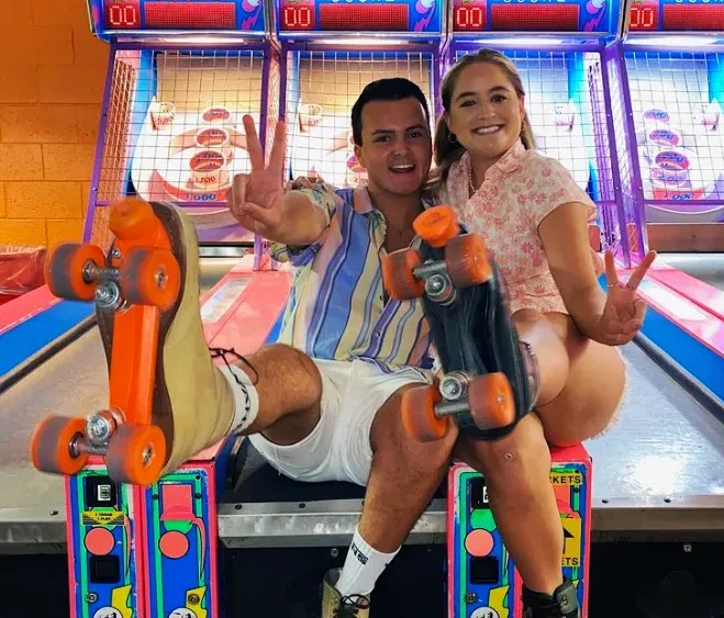 couple sitting on skee ball game holding out their skates and showing piece signs